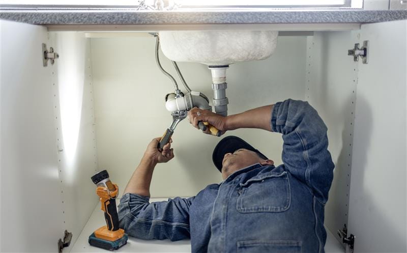 Plumber repairing pipes beneath a bathroom sink in Haines City