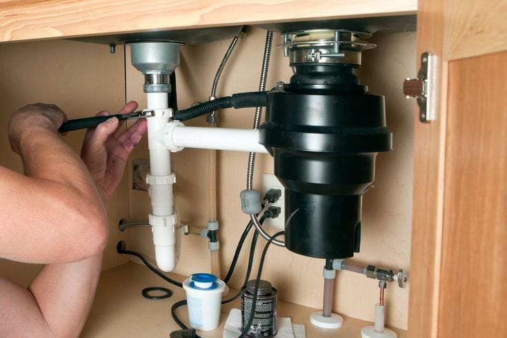 Plumber installing a garbage disposal beneath a kitchen sink in Haines City