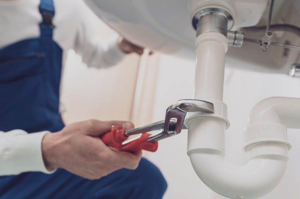 Plumber repairing a white drain pipe beneath a sink in Haines City